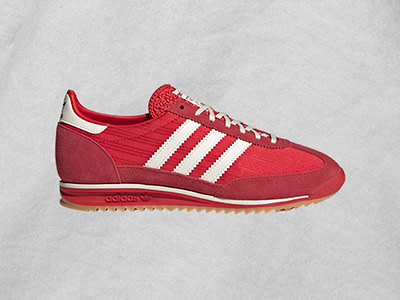 Ένα κόκκινο και λευκό adidas sneaker με σόλα από φυσικό καουτσούκ εμφανίζεται σε ανοιχτό γκρι φόντο.