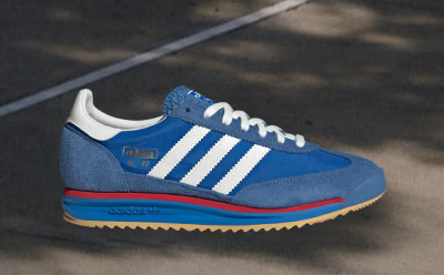 A blue and white Adidas sneaker with red accents sits on a dark surface, with a blurred background suggesting an outdoor setting.