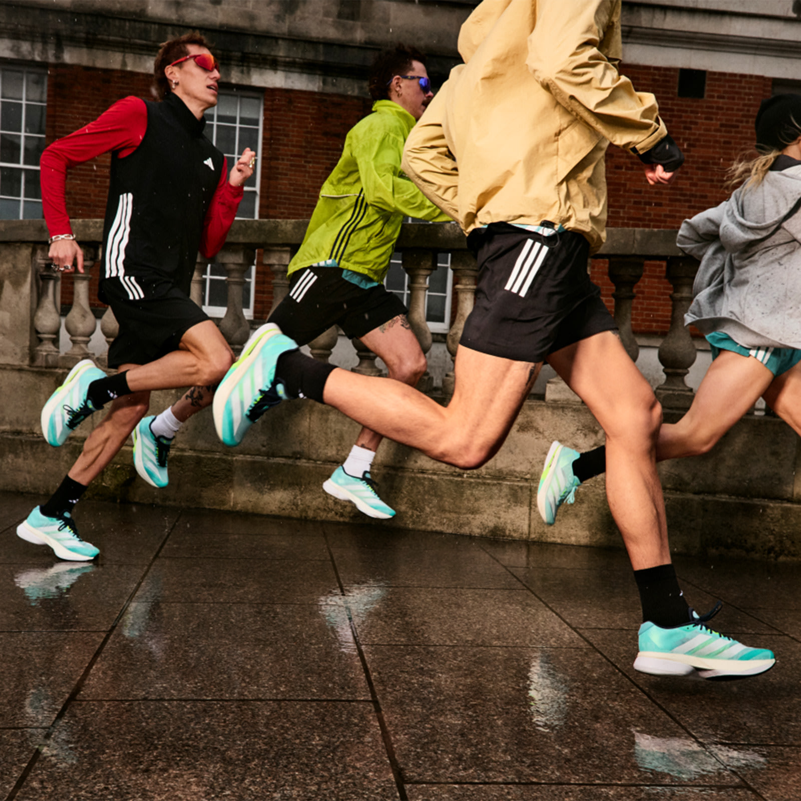A group of people in athletic clothing are running up a set of stairs in an urban setting, with a brick building visible in the background.