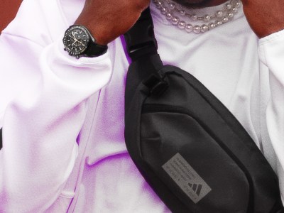A close up of a person with a hood up wearing a black adidas cross body bag.