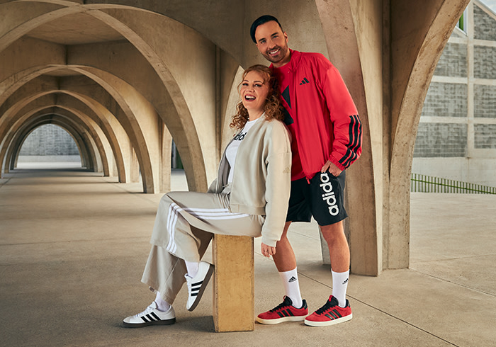 A man and a woman, both wearing casual athletic attire, stand together in an arched hallway with a stone-like interior.