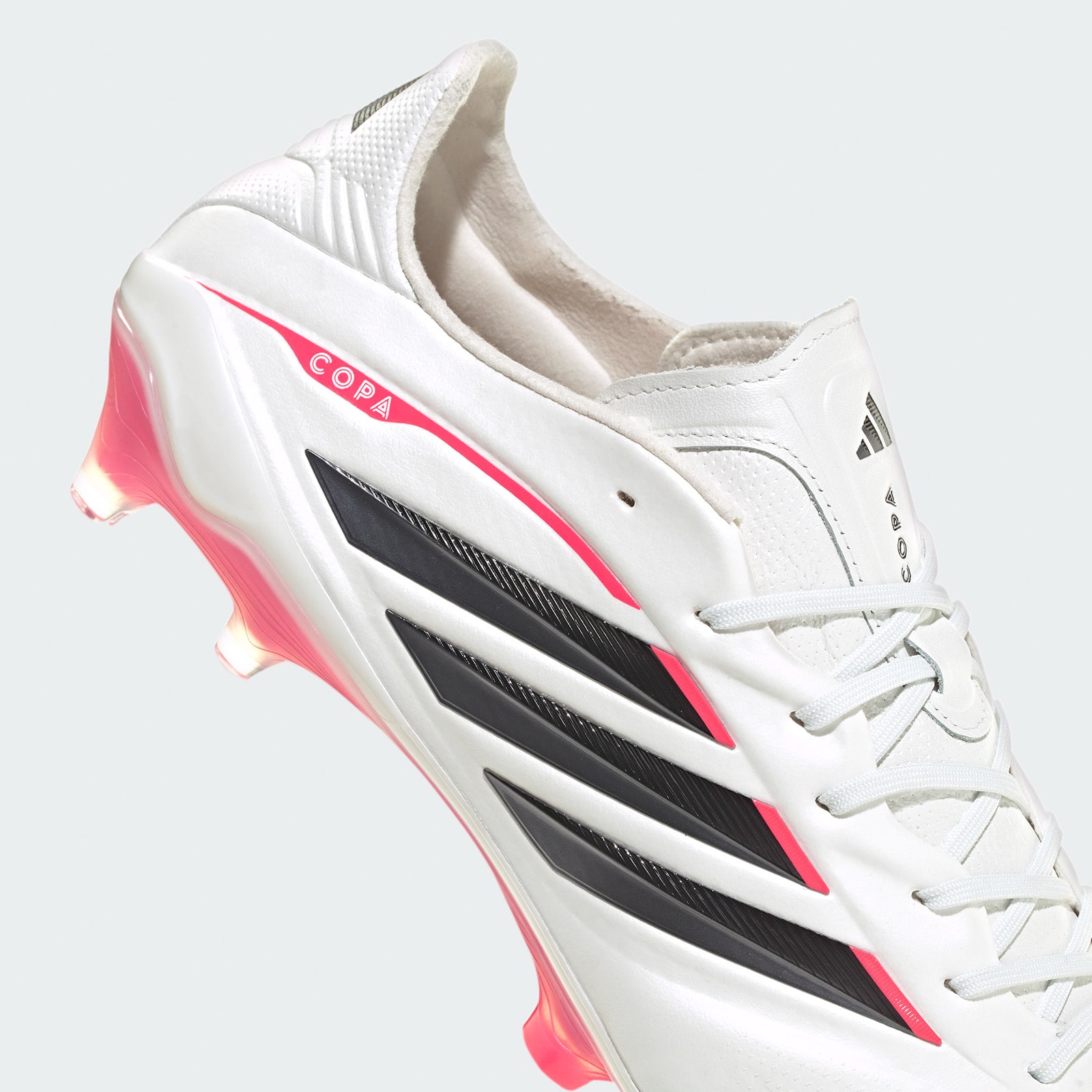 A white and pink Adidas soccer cleat with black stripes and a textured sole, against a plain white background.