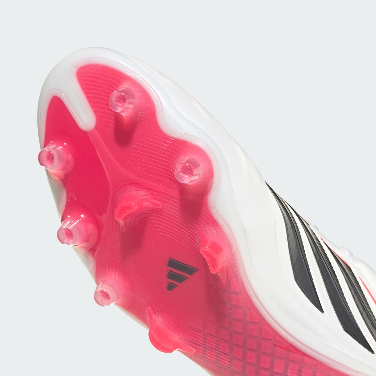 A close-up view of a white and pink sports shoe with a textured sole and studs, set against a plain white background.