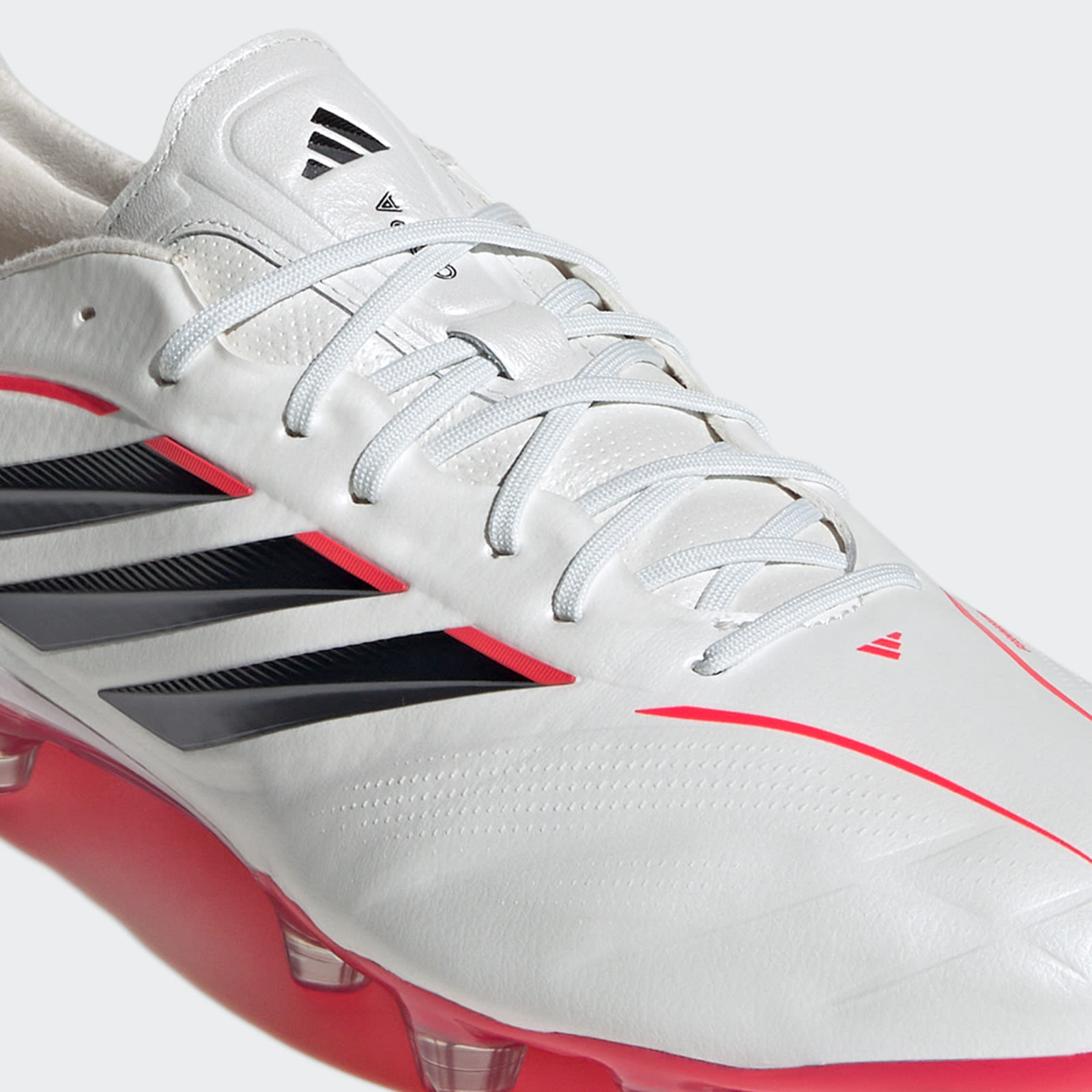 A close-up view of a pair of white and red Adidas soccer cleats with black stripes and accents, set against a plain background.