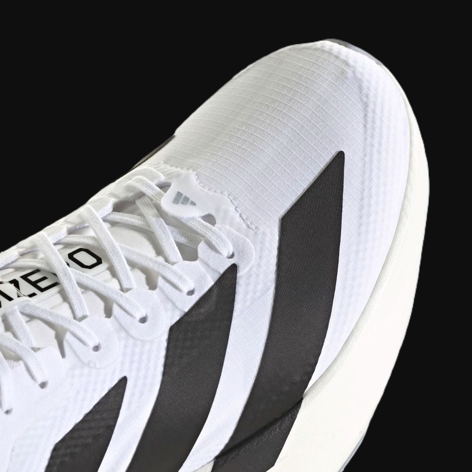 A close-up view of a white and black athletic shoe with intricate lacing and a textured sole against a dark background.