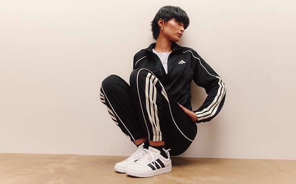 A person wearing a black and white striped jacket and white sneakers stands against a plain beige background.