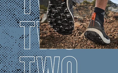 Das Bild zeigt die Füße einer Person, die auf einem unbefestigten Trail Sportschuhe trägt, mit einem blau-weißen Grafikdesign im Hintergrund.