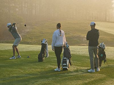 A group of golfers stands on a misty golf course, their golf bags and clubs visible as they prepare to play.