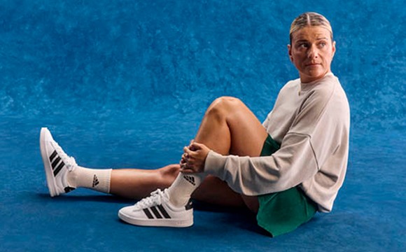 A person wearing a white shirt and Adidas sneakers sits on the floor against a vibrant blue background.