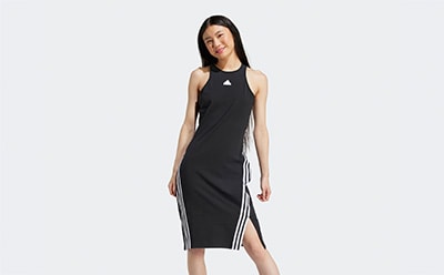 A young woman wearing a black sleeveless dress with white stripes stands against a plain white background, smiling confidently.