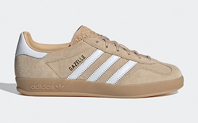 A pair of beige and white Adidas Gazelle sneakers with a gum sole, set against a plain white background.