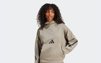 The image shows a person wearing a beige hooded sweatshirt with the Adidas logo, standing against a plain white background.