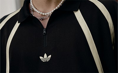 A close-up view of a person wearing a black and white striped jacket, with a pearl necklace visible and the Adidas logo prominently displayed on the jacket.
