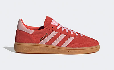 A pair of red and pink Adidas sneakers with a gum sole sits on a plain background.