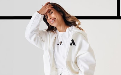 A young woman with long, wavy hair is smiling and covering her face with her hands in a white, minimalist setting.