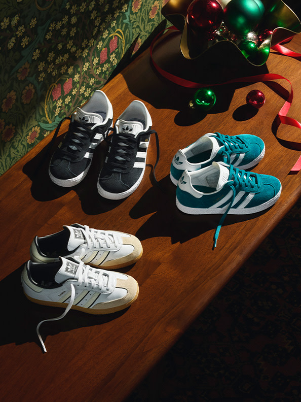 A collection of various sneakers and holiday ornaments rests on a wooden surface, with a patterned fabric backdrop providing a festive atmosphere.