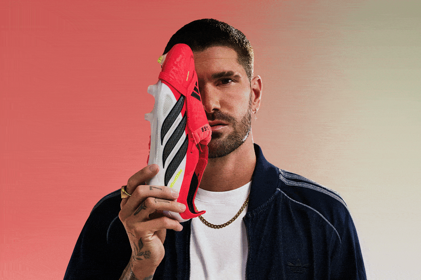 A man with a beard and tattoos holds a red and white striped object in front of his face against a solid coral-colored background.