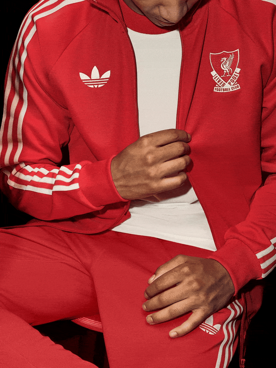 A person wearing a red Adidas tracksuit with the Liverpool FC logo, sitting against a dark background.