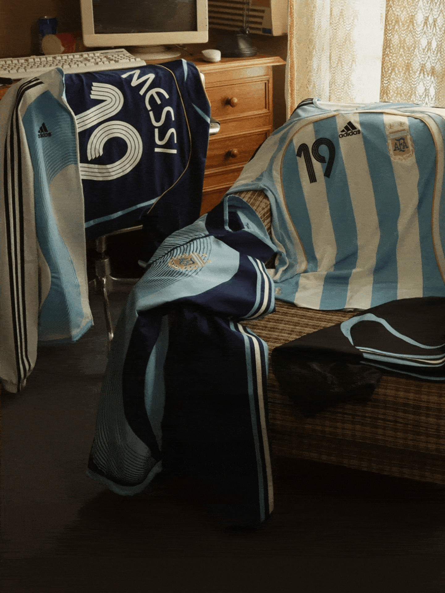 The image shows various sports jerseys and equipment, including a navy blue jersey with the number 5 and the word "Messi" on it, as well as a striped jersey with the number 19. The jerseys are placed on a wooden dresser or cabinet in what appears to be a bedroom or living space.