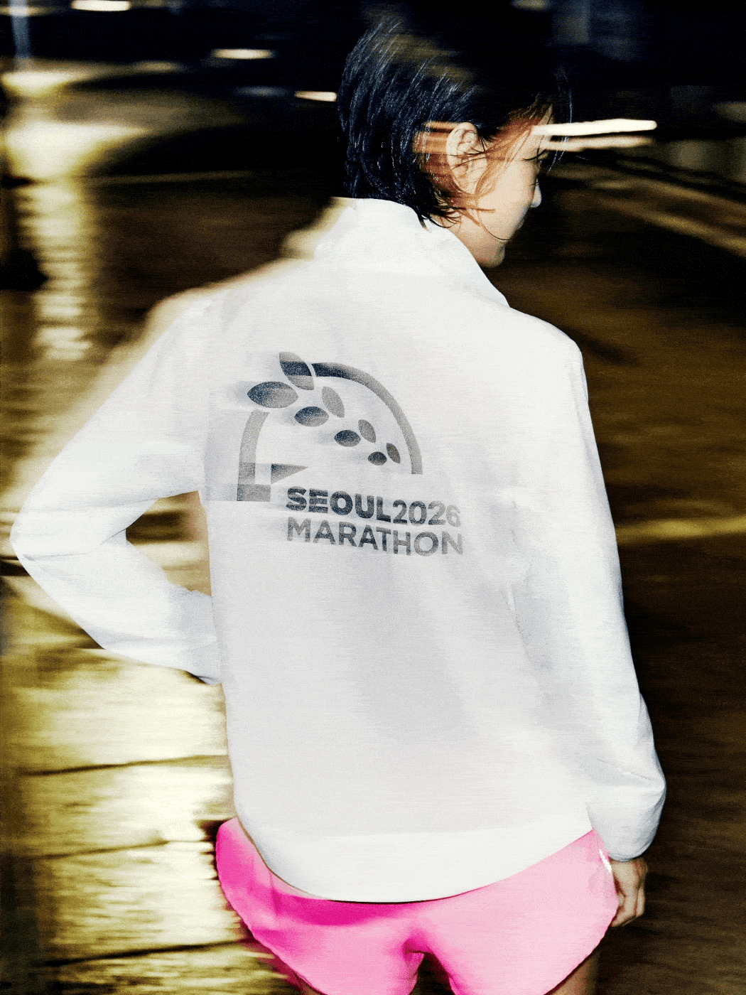 A person wearing a white shirt with the "Seoul 2022 Marathon" logo is walking in a dimly lit environment, with blurred surroundings suggesting a nighttime setting.