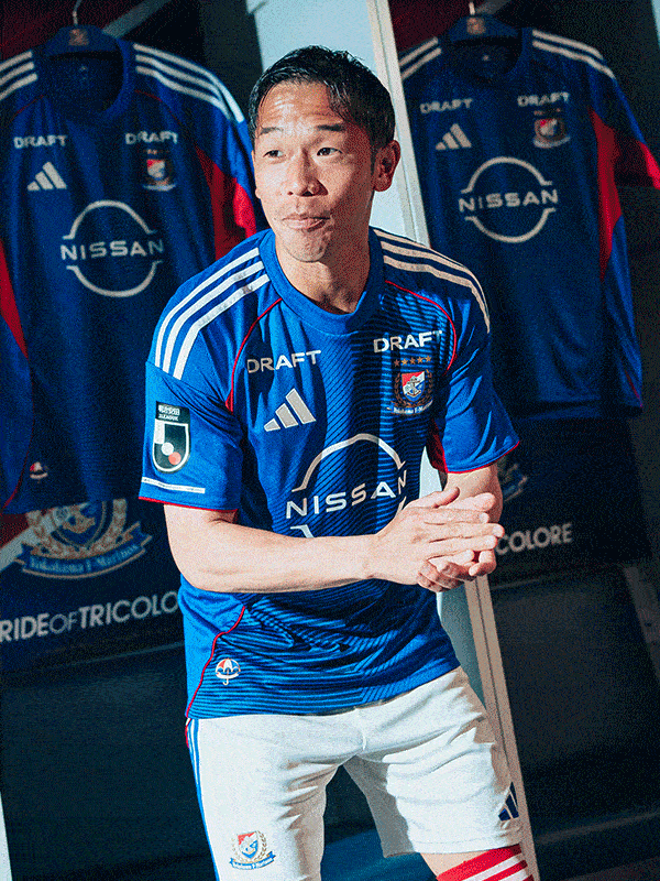 The image shows a man wearing a blue and white soccer jersey with the Nissan logo, standing in front of a display of additional jerseys.