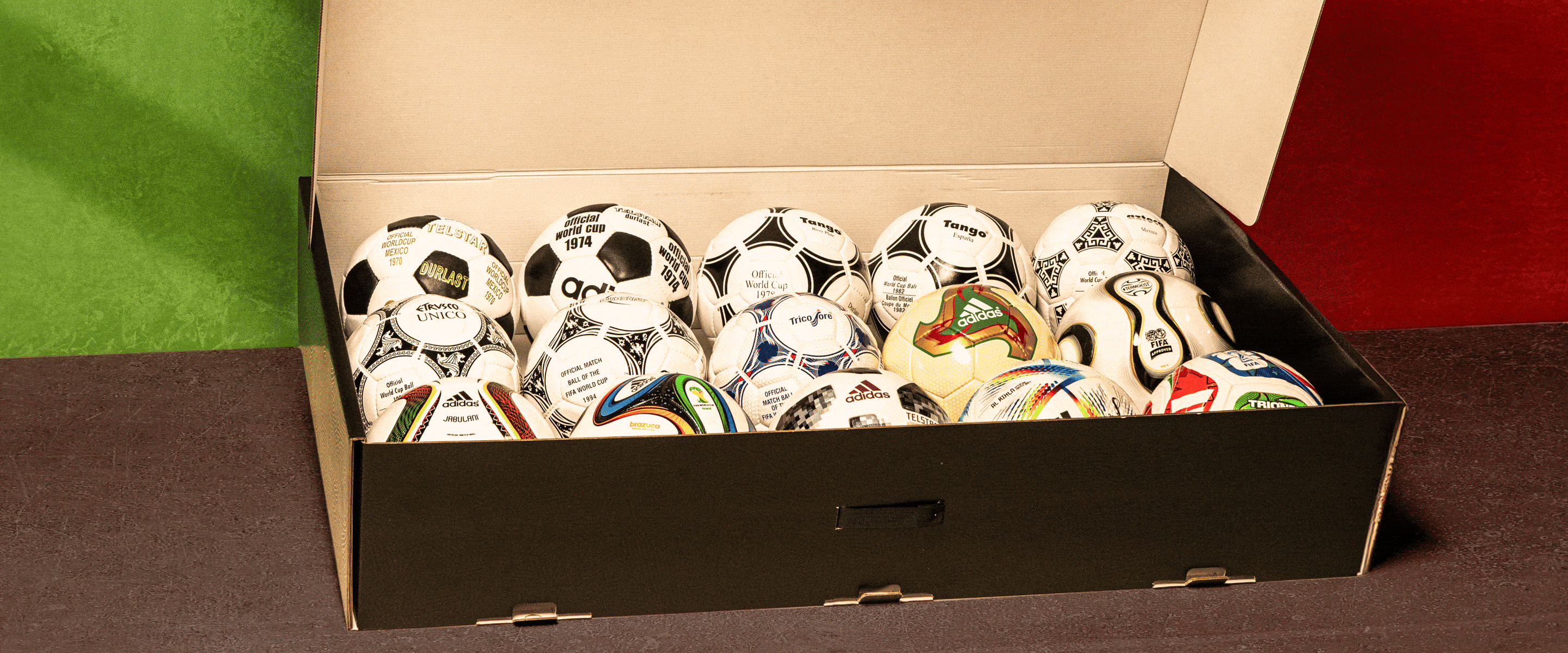 A box filled with various soccer balls of different designs and colors, placed against a plain background.