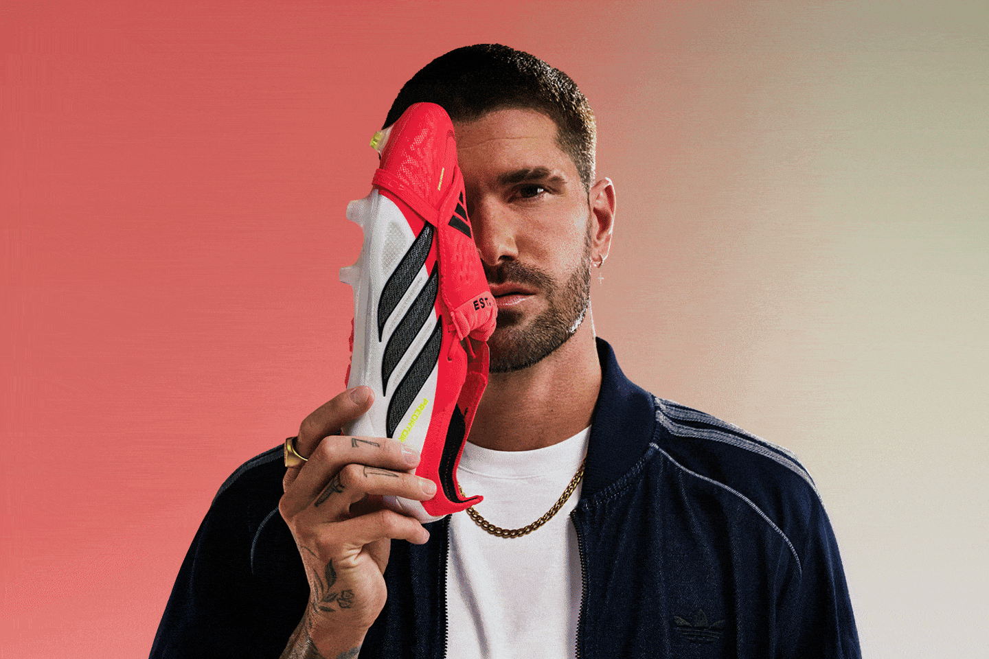 A man with a beard and tattoos holds a red and white striped object in front of his face against a solid coral-colored background.