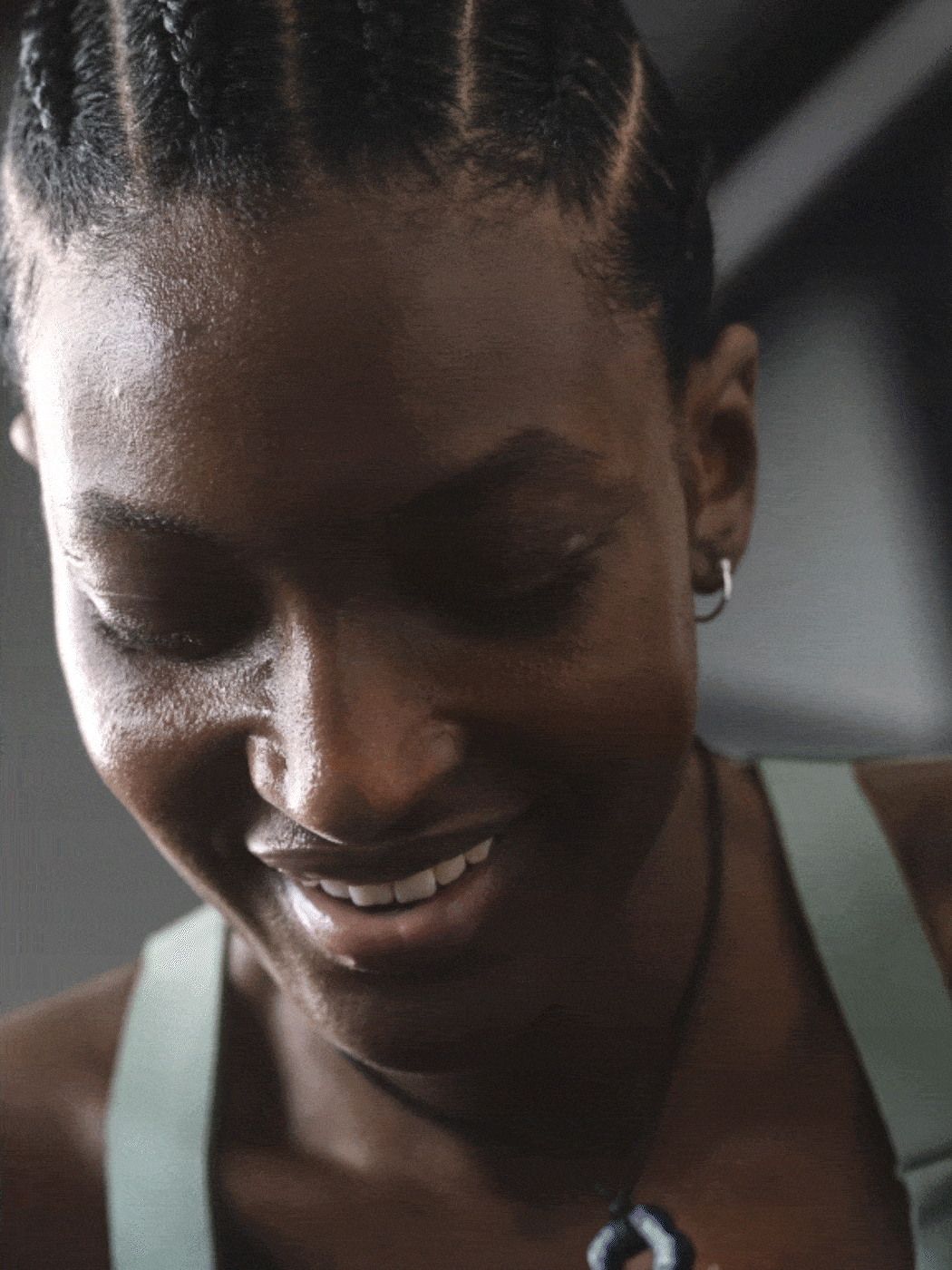 A close-up portrait of a smiling young woman with dark skin and braided hair, set against a blurred background.