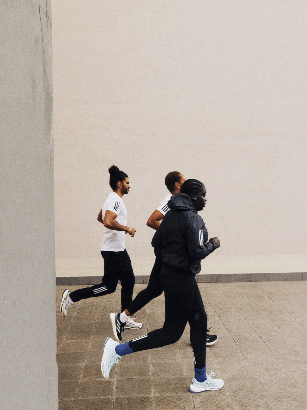 Two individuals in athletic attire are running together in an indoor setting with a plain white wall in the background.