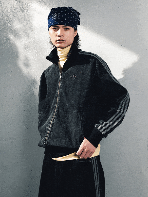 A person wearing a black jacket and a patterned hat stands in front of a blurred, snowy background.