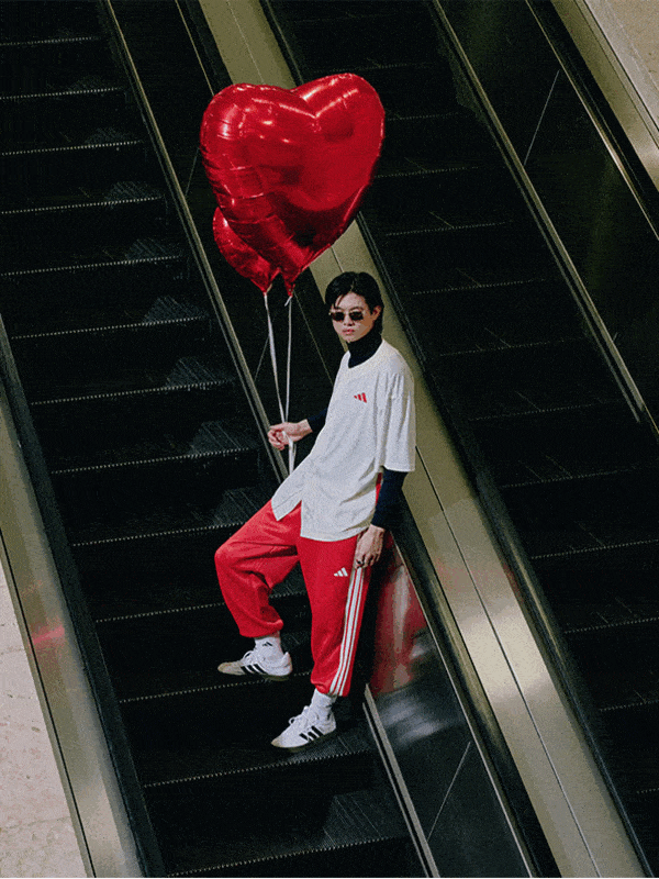 A person in a white shirt and red pants stands on an escalator, holding a large red heart-shaped balloon.