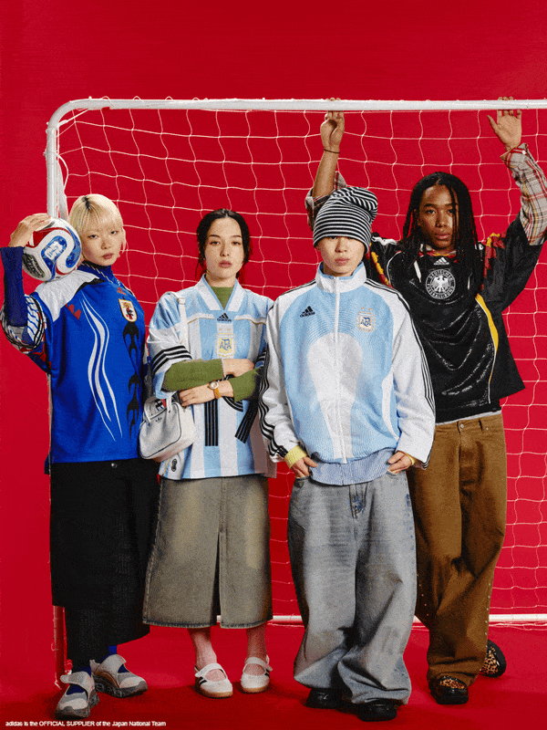 A group of young individuals, dressed in various sports and casual attire, stand in front of a red backdrop with a soccer goal net.