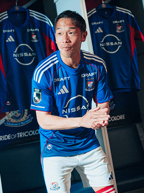 The image shows a man wearing a blue and white soccer jersey with the Nissan logo, standing in front of a display of additional jerseys.