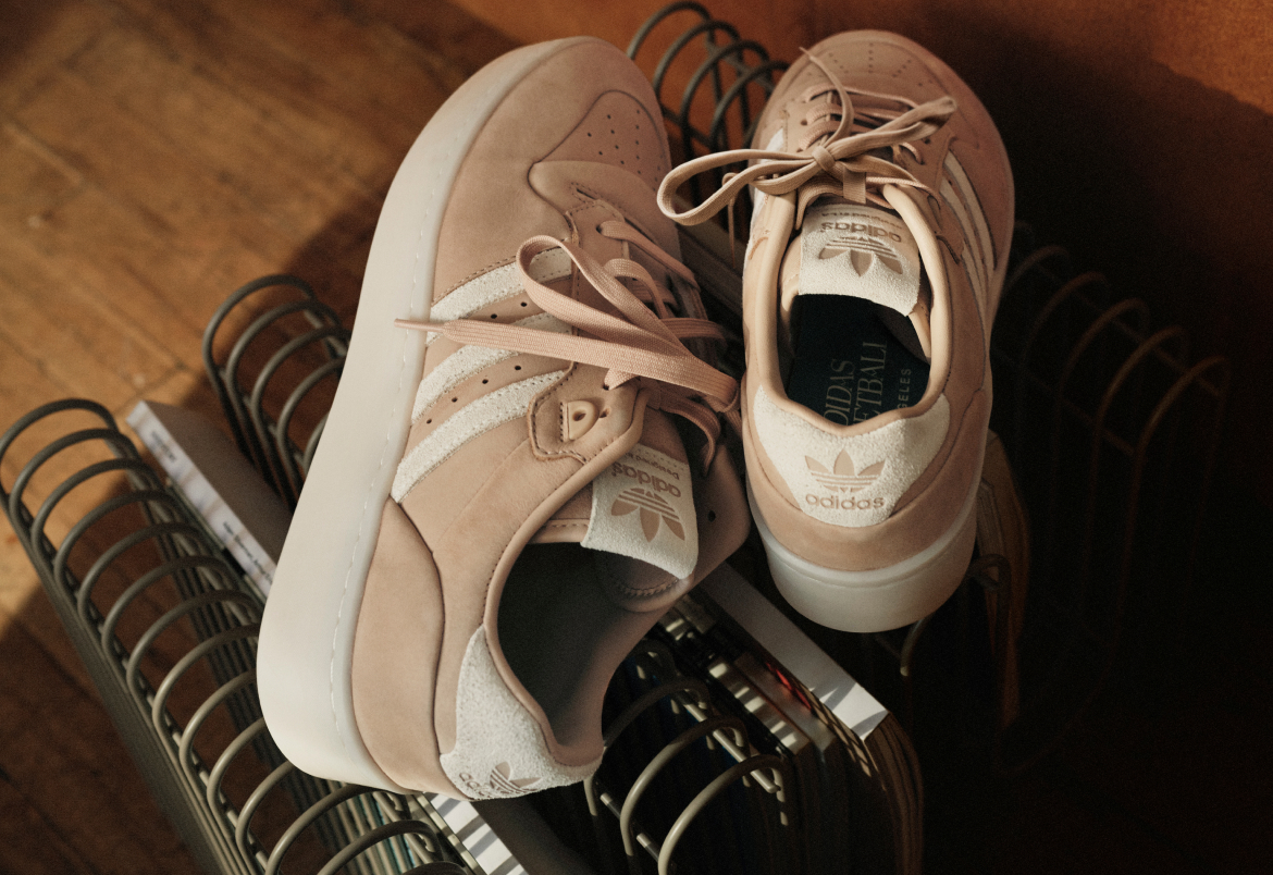 A pair of white and beige sneakers with laces sit on a metal rack, surrounded by other shoes in the background.