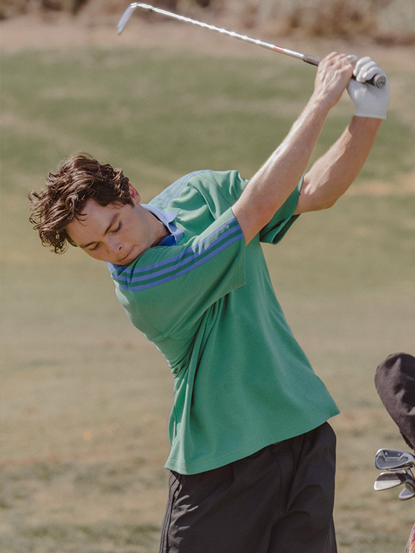 A young person in a green shirt is swinging a golf club on a grassy field.