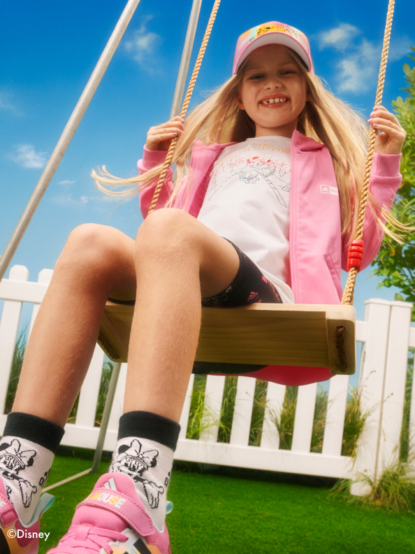Girl on swing smiling wearing the adidas | Minnie Mouse collection
