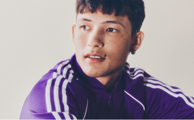 A portrait of a man with black hair wearing a purple adicolor tracksuit in front of a white backdrop. 
