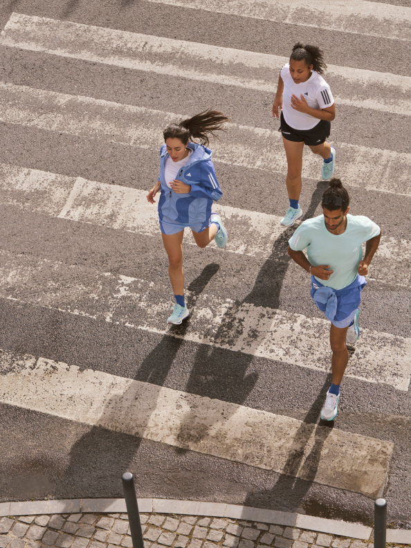 Three people in adidas running apparel and Supernova shoes running across a sunlit asphalt road.