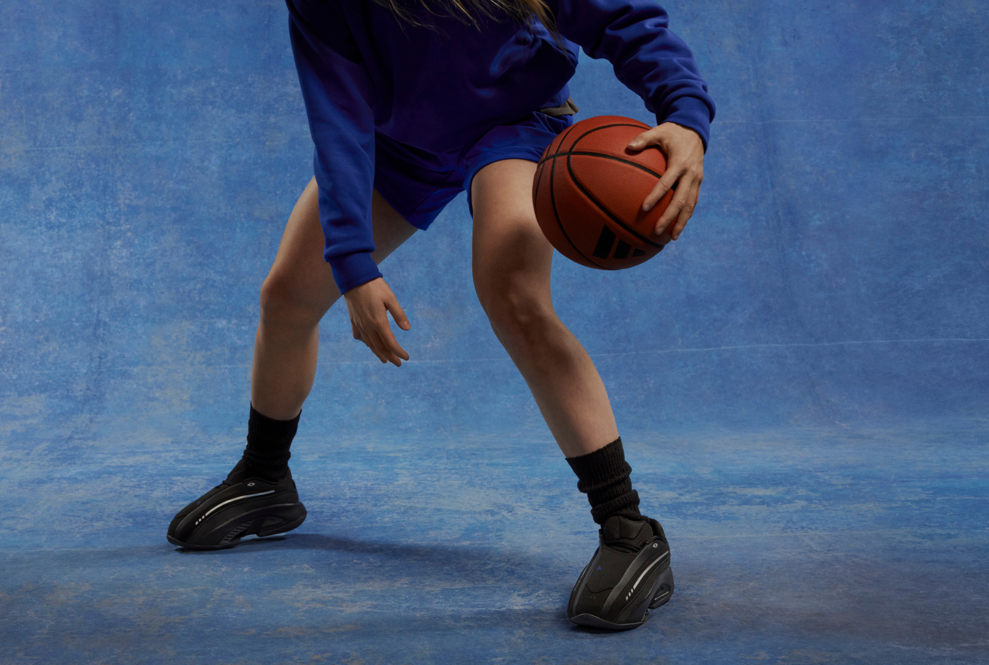 Close-up of person in a blue sweatshirt and shorts holding a basketball.