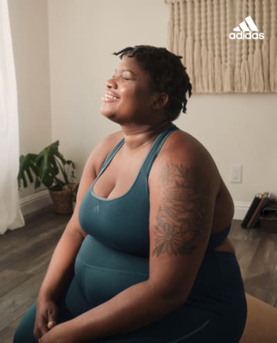 A woman wearing a teal yoga tank top smiles peacefully in a seated yoga pose.