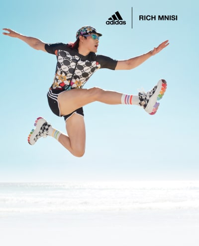 A male model jumps, mid-air, at the beach, styled in apparel from adidas x Rich Mnisi Pride Collection.