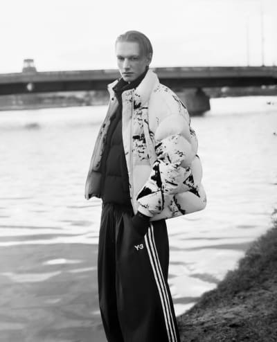 A black and white images captures a model in front of a riverside backdrop.