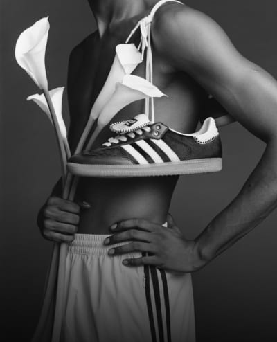 A model is posing wearing the adidas Originals by Wales Bonner collection with flowers in one hand, and the other hand on their hip.