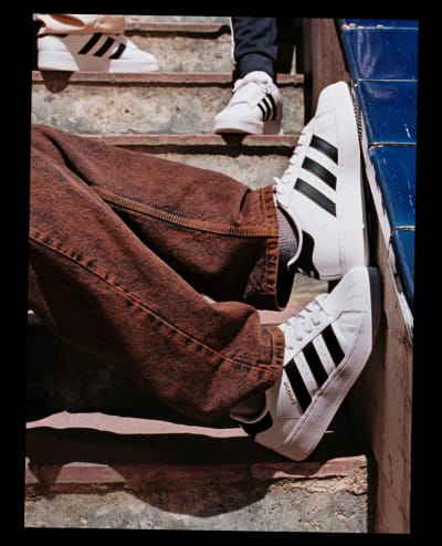 The legs of a model sitting on concrete stairs, wearing the adidas Superstar XLG with the black 3-Stripes facing the camera.