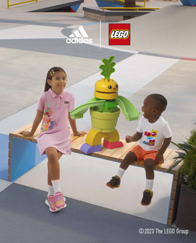 A little girl and infant boy sitting on a bench with a DUPLO® carrot character.