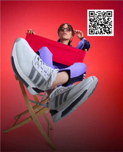 Zoom crop of actress Jenna Ortega sitting in director chair wearing adidas tracksuit and sneakers.