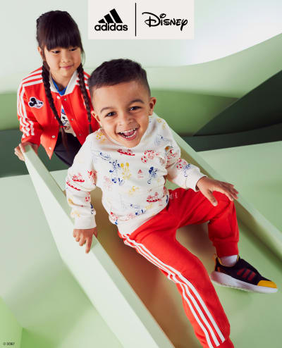 Two children going down a slide both wearing the adidas | Mickey and Friends collection.