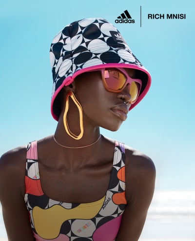 A male model jumps, mid-air, at the beach, styled in apparel from adidas x Rich Mnisi Pride Collection.