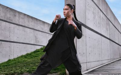 A woman with black hair wears all-black Y-3 apparel while posing in nature.