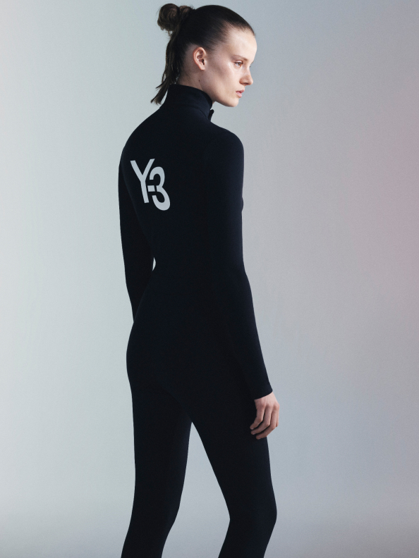 A woman with slicked-back hair poses in a white adidas Y-3 jacket and matching pants against a white backdrop.